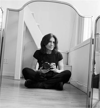 Charilyn Zlotnik, self-portrait seated on the floor with camera, reflected in mirror, black-and-white photograph.