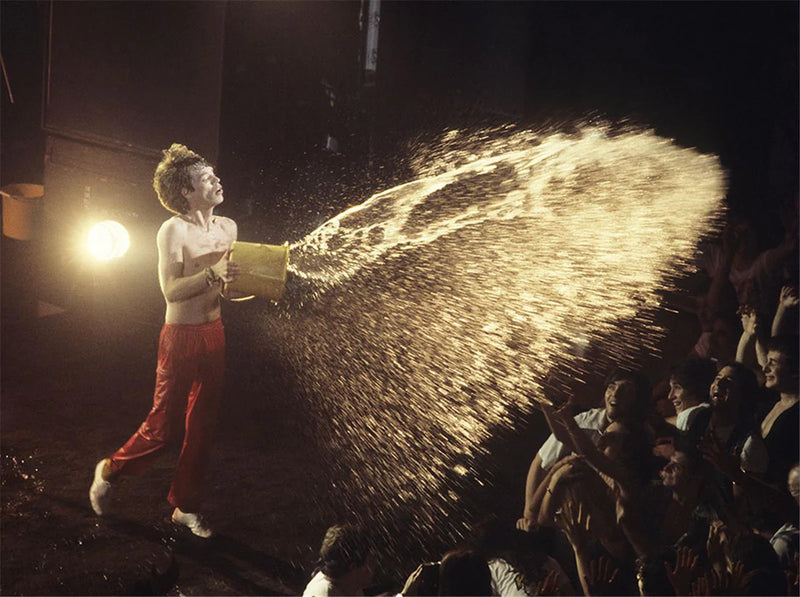 Mick Jagger of the Rolling Stones pouring water over the audience during a live performance at The Palladium, New York City, 1978, photograph by Charilyn Zlotnik.
